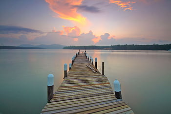 Tranquil view of a wooden pier extending into the calm lake during a breathtaking sunset. HD wallpaper