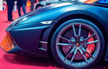 Detailed view of a luxury sports car wheel on a red carpet at an auto show. HD wallpaper