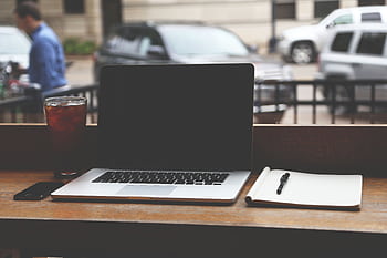 MacBook Pro on a wooden table with iced coffee and notebook in a casual coffee shop setting. HD wallpaper