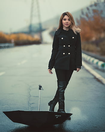 Stylish woman in black coat and boots stands with umbrella on a rainy street. HD phone wallpaper