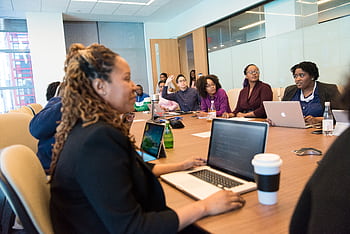 A diverse group of professionals engaging in a team meeting with laptops and discussions in a modern office setting. HD wallpaper