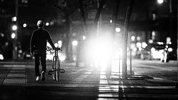 Silhouette of a person walking a bicycle on a city sidewalk at night. HD wallpaper