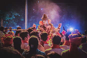 A vibrant night scene of people celebrating Ganesh Chaturthi with a beautifully adorned Ganesha idol. HD wallpaper