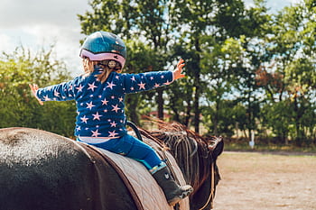 A child confidently rides a horse outdoors, wearing a helmet and star-patterned jacket. HD wallpaper