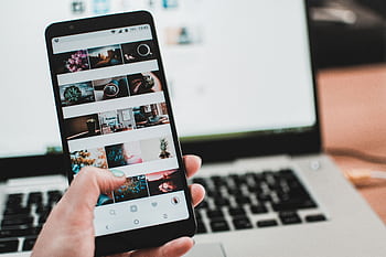 A person uses a smart to browse social media in front of a laptop, emphasizing modern technology and lifestyle. HD wallpaper