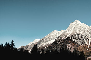 Breathtaking view of snow-capped mountains and forest at sunrise, ideal for adventure seekers. HD wallpaper