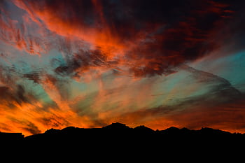 Stunning sunset with vibrant orange and blue hues casting silhouettes over mountain horizon. HD wallpaper