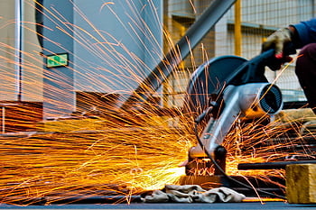 A worker operates a grinder cutting metal, creating a vibrant display of sparks in an industrial setting. HD wallpaper