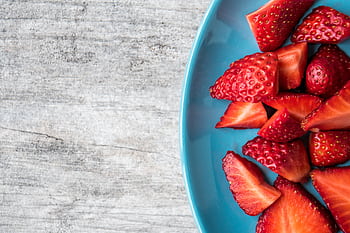 A close-up of fresh organic strawberries sliced on a blue plate for a healthy snack. HD wallpaper