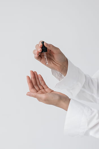 A person's hands applying skincare serum using a dropper for a beauty routine. HD phone wallpaper