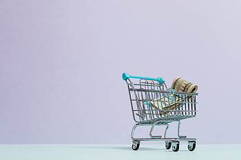A close-up of a mini shopping cart with rolled cash on a pastel background. Ideal for finance and ecommerce themes. HD wallpaper