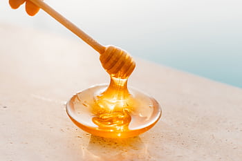 Golden honey flowing from a wooden dipper onto a glass plate, captured in warm daylight. HD wallpaper