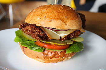Delicious crispy chicken burger with fresh veggies and cheese on a sesame seed bun, served on a plate. HD wallpaper