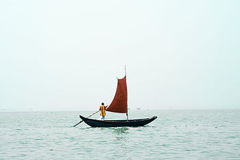 A lone fisherman sails a traditional boat on a serene Bangladesh waterway at sunrise. HD wallpaper