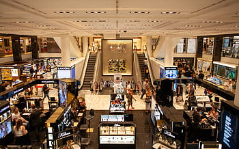 A bustling scene inside a modern shopping mall with escalators and various retail stalls. HD wallpaper