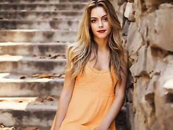 A beautiful woman with long blonde hair and red lips posing by a stone wall outdoors. HD wallpaper
