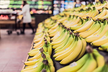 Rows of ripe bananas displayed attractively in a supermarket aisle. HD wallpaper
