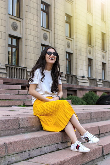 Smiling young woman in a yellow skirt sitting on steps in Almaty, Kazakhstan. HD phone wallpaper