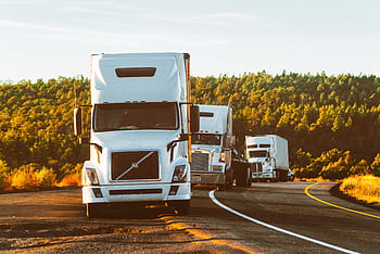 Three semi trucks driving on a highway through a forested landscape in Arizona. HD wallpaper