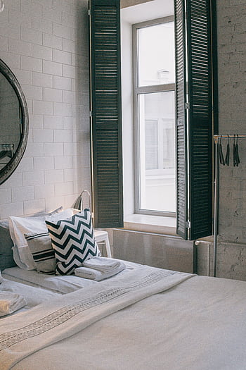 A cozy and stylish bedroom featuring modern decor and a sunlit window with shutter panels. HD phone wallpaper