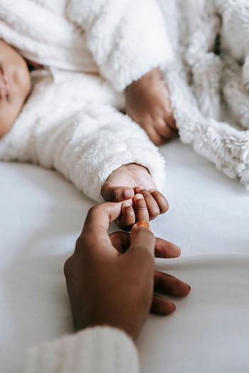 A serene scene of a mother holding her sleeping baby's hand in warm clothes. HD phone wallpaper