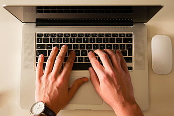 Hands typing on a laptop keyboard, showcasing a modern workplace environment with a mouse nearby. HD wallpaper