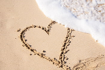 A heart drawn in sand with ocean waves approaching, symbolizing love and nature. HD wallpaper