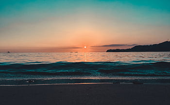 A stunning sunset over a tranquil beach with reflective waters and gentle waves, creating a peaceful seascape. HD wallpaper