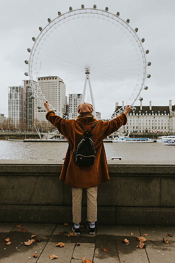 Person with arms raised viewing the London Eye across River Thames in autumn. HD phone wallpaper
