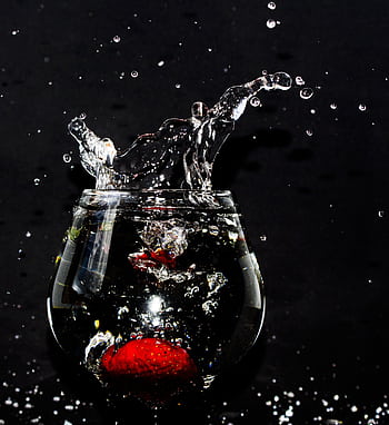 A strawberry splashes into a glass of water, creating dynamic droplets against a black background. HD phone wallpaper
