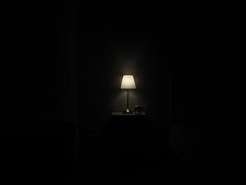 Illuminated lamp on nightstand casting a warm glow in a dark, minimalist room. HD wallpaper