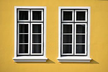 Two white-framed windows on a vibrant yellow building facade in Büsum, Germany. HD wallpaper