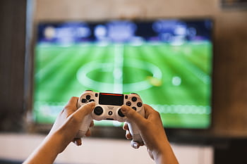 Close-up of hands holding a game controller playing a football video game on screen. HD wallpaper