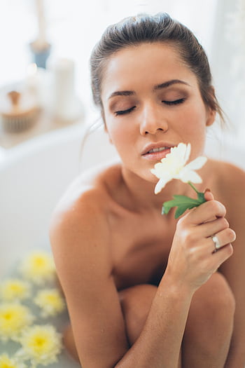 A woman enjoying a relaxing spa bath, surrounded by white flowers, embracing tranquility and self-care. HD phone wallpaper
