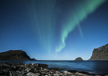 A breathtaking view of the aurora borealis above the rocky coast of Lofoten, Norway at night. HD wallpaper