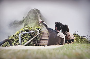 A young couple enjoys the scenic view from a foggy mountain stairway, embracing nature's beauty. HD wallpaper