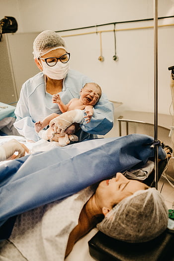 A doctor holds a newborn baby in a hospital setting post-delivery. HD phone wallpaper