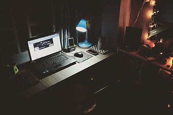 A well-lit desk with a laptop and modern accessories, capturing a cozy nighttime work environment. HD wallpaper