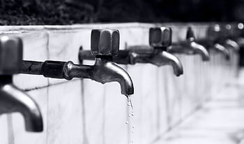Black and white of a row of faucets with water dripping, highlighting plumbing details. HD wallpaper