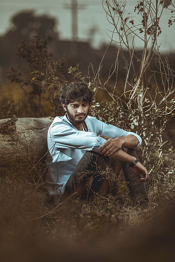 A thoughtful young man sitting outdoors surrounded by vegetation, deep in thought. HD phone wallpaper
