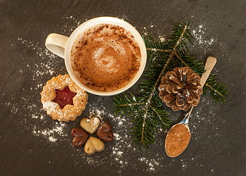White mug of hot chocolate with festive cookies, pinecone, and cinnamon on a dark surface. HD wallpaper