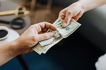 A close-up of hands exchanging US dollar bills, symbolizing financial transaction or payment. HD wallpaper