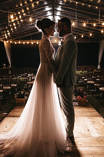Elegant bride and groom embracing under twinkling string lights, capturing a romantic moment. HD phone wallpaper