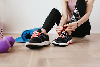 Fit woman tying shoelaces, preparing for indoor workout with yoga mat and dumbbells. HD wallpaper