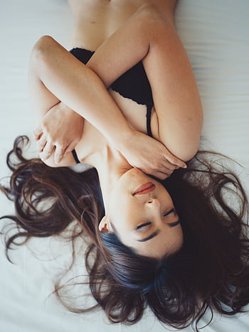 A serene young woman in lingerie relaxing on a bed with tousled hair. HD phone wallpaper