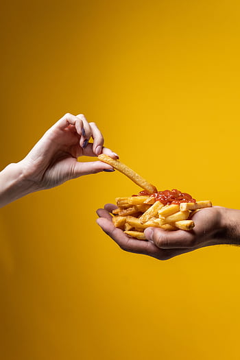 A close-up of hands sharing a delicious pile of french fries with ketchup against a yellow background. HD phone wallpaper
