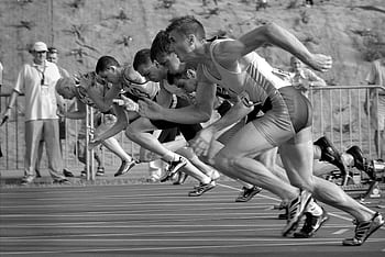 Athletes burst from the blocks during a sprint race, captured in monochrome. HD wallpaper