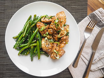 A delicious serving of sesame chicken with fresh green beans on a white plate, perfect for dinner. HD wallpaper