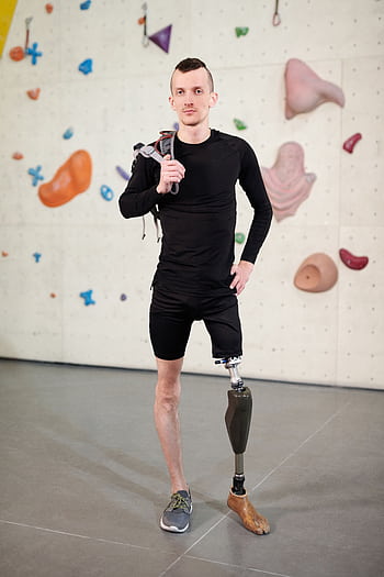 Young man with prosthetic leg confidently posing at indoor climbing gym, showcasing determination and strength. HD phone wallpaper