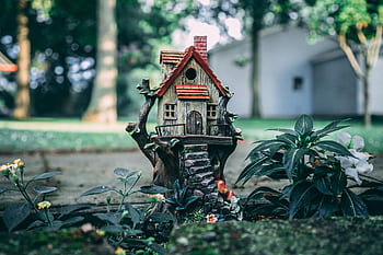 A whimsical miniature house set amidst a lush fairy garden, evoking a sense of enchantment and fantasy. HD wallpaper